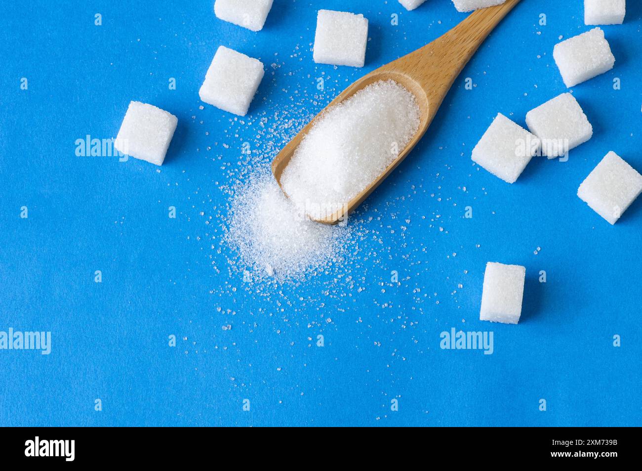 Haufen weißen Kristallzuckers mit Zuckerwürfel auf blauem Hintergrund Stockfoto