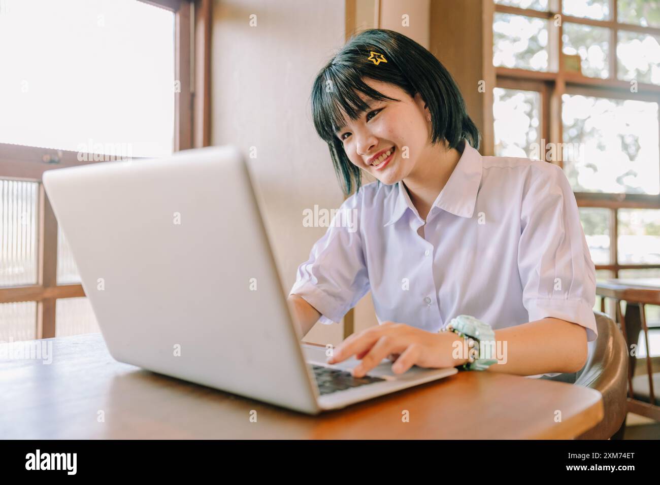 Junge asiatische Schule Teenager Mädchen Uniform sitzt mit Laptop Computer glücklich lächelnd im Café Stockfoto