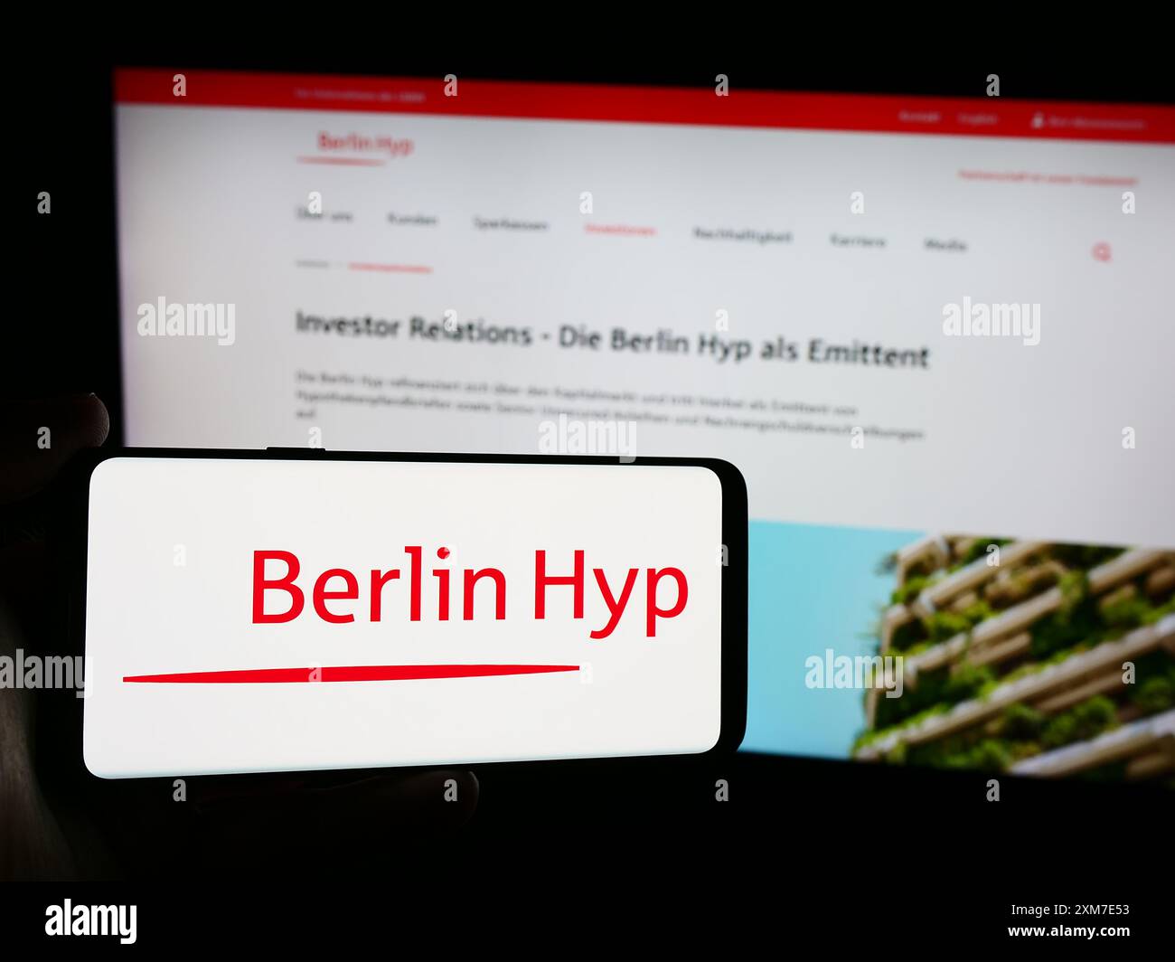 Person mit Mobiltelefon mit Logo der deutschen Hypothekenbank Berlin Hyp AG vor der Business-Webseite. Schwerpunkt auf dem Display des Telefons. Stockfoto