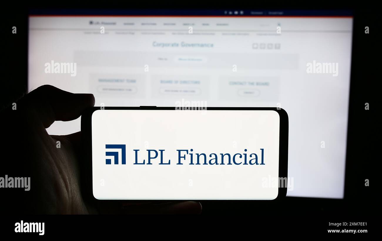 Person, die ein Mobiltelefon mit dem Logo der US-amerikanischen Broker-/Händlerfirma LPL Financial Holdings Inc. Vor der Website des Unternehmens hält. Schwerpunkt auf dem Display des Telefons. Stockfoto