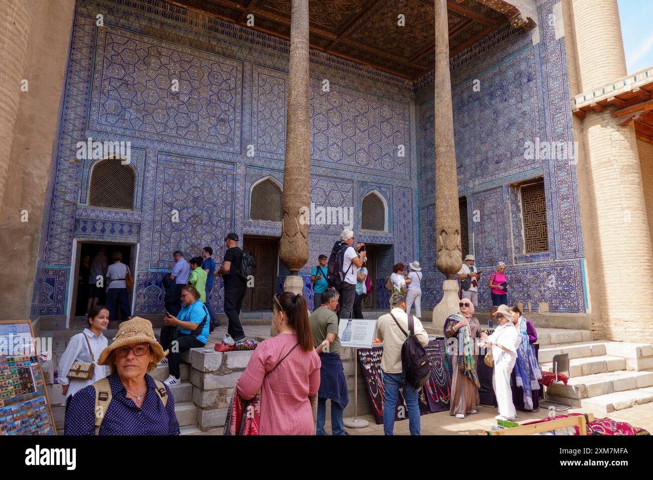 Eine Gruppe von Touristen erkundet die Ak-Sheikh-Bobo-Moschee mit komplexen blauen Fliesen und hohen Holzsäulen in Chiwa, Usbekistan Stockfoto
