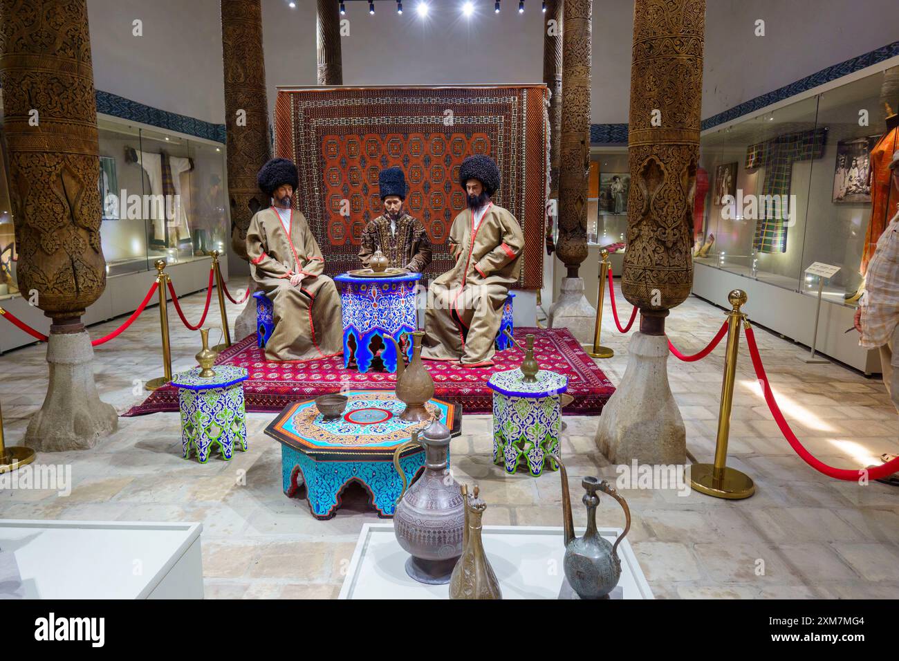 Traditionelle kulturelle Ausstellung von Männern in regionaler Kleidung um einen Tisch in einem historischen Museum mit kunstvoller Dekoration und Artefakten in Usbekistan Stockfoto