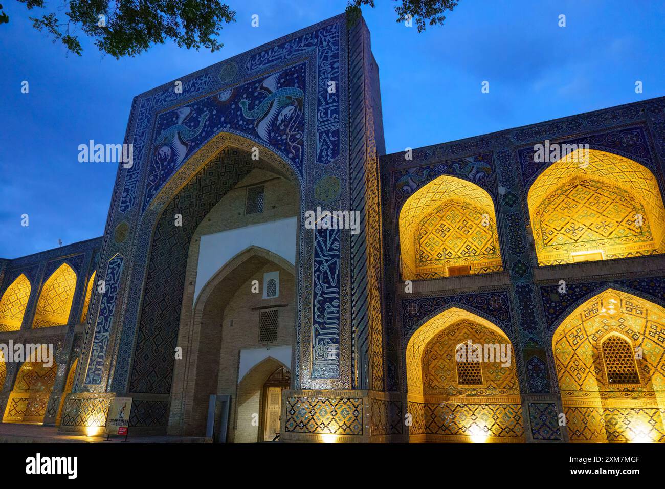 Beleuchtete Fassade der historischen mir-i-Arab Madrasa in Buchara, Usbekistan, in leuchtenden roten, blauen und gelben Lichtern in der Abenddämmerung Stockfoto