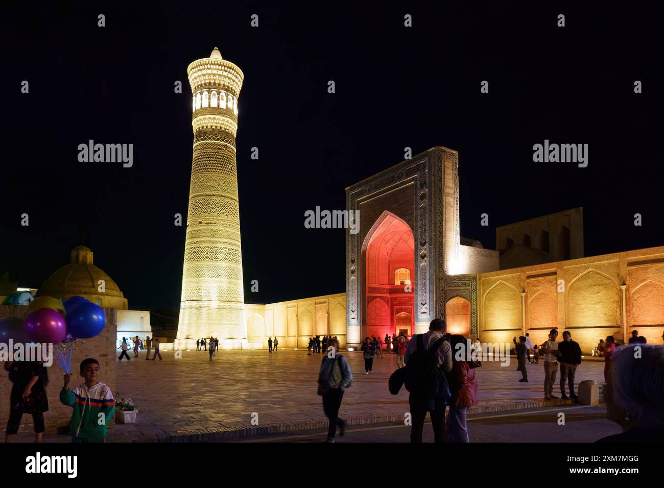 Abendlicher Blick auf das beleuchtete Kalyan Minarett und den Moscheen-Innenhof in Buchara, Usbekistan, mit Menschen, die spazieren gehen und Fotos machen Stockfoto