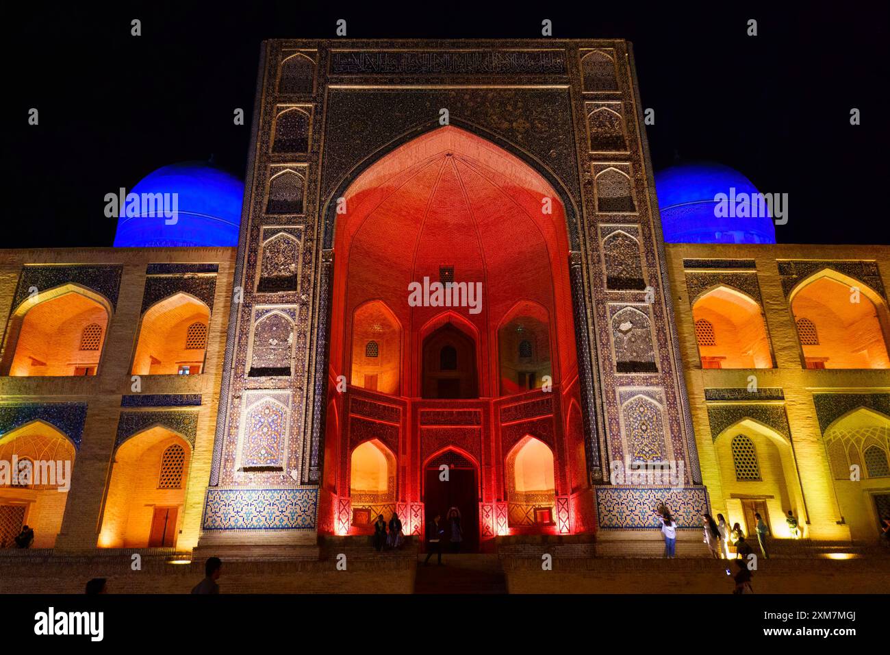Beleuchtete Fassade der historischen mir-i-Arab Madrasa in Buchara, Usbekistan, die nachts in leuchtenden roten, blauen und gelben Lichtern leuchtet Stockfoto