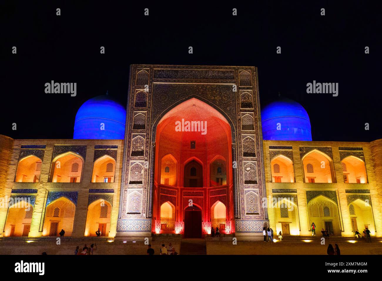 Beleuchtete Fassade der historischen mir-i-Arab Madrasa in Buchara, Usbekistan, die nachts in leuchtenden roten, blauen und gelben Lichtern leuchtet Stockfoto
