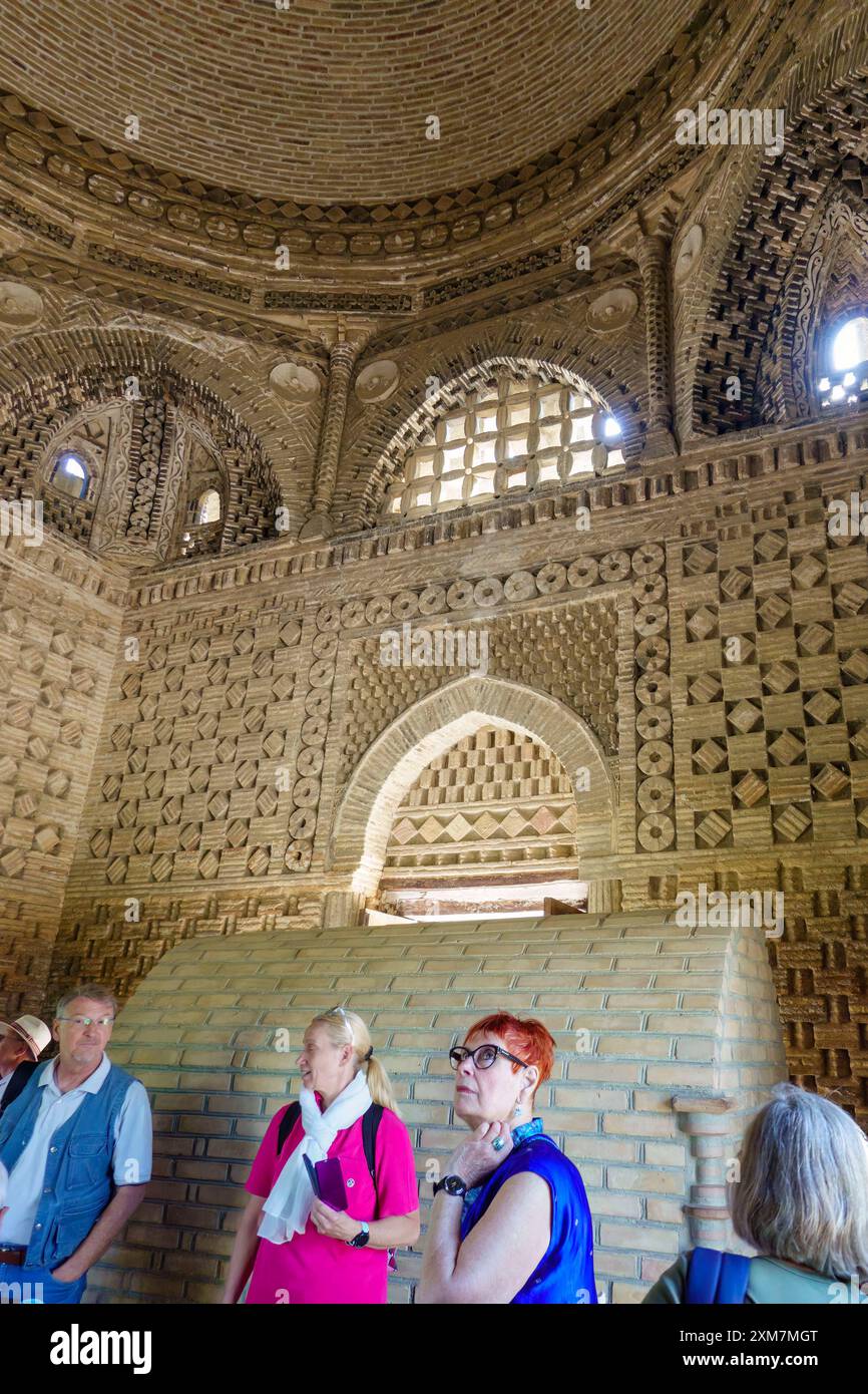 Touristen erkunden das komplizierte Innere eines alten Ziegelmausoleums mit detaillierten geometrischen Mustern und Bogenfenstern in Usbekistan Stockfoto