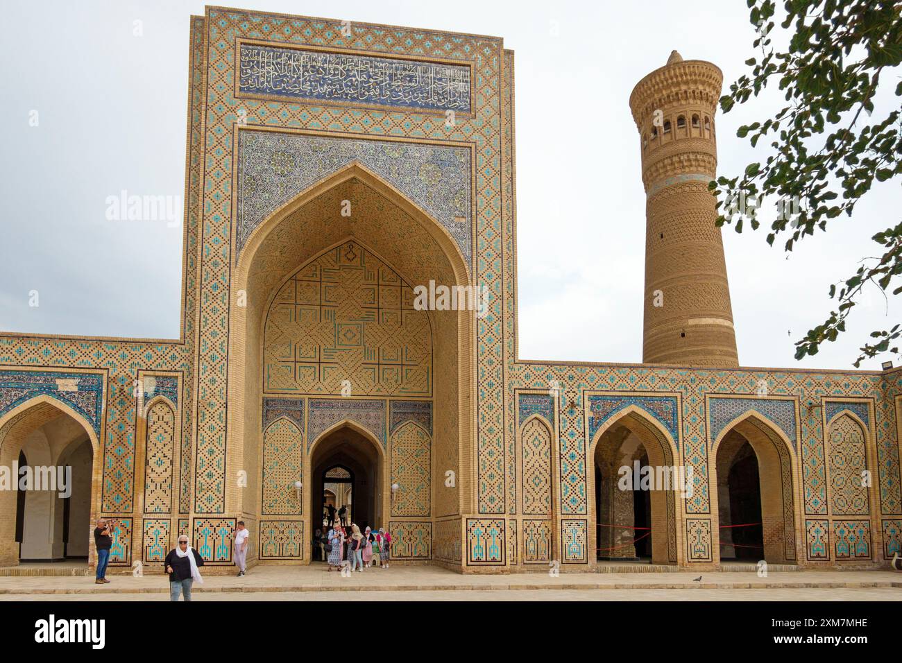 Besucher treffen sich am Eingang der historischen Kalyan Moschee mit komplexen Mosaikfliesen und einem riesigen Minarett in Buchara, Usbekistan Stockfoto