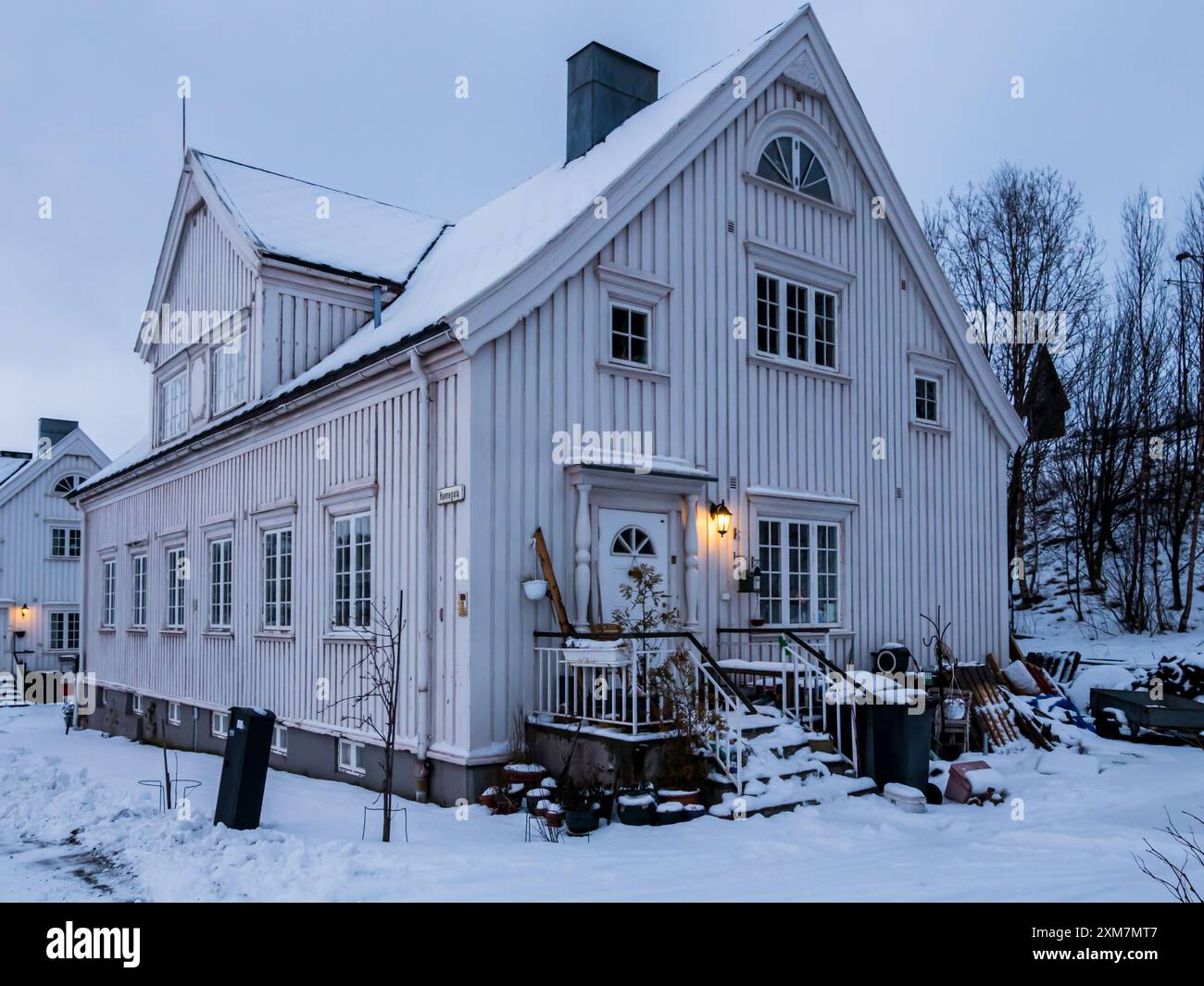 Narvik, Norwegen - Februar 2023: Straße mit weißen Holzhäusern, die in der Abenddämmerung mit Schnee bedeckt sind. Nordeuropa Stockfoto