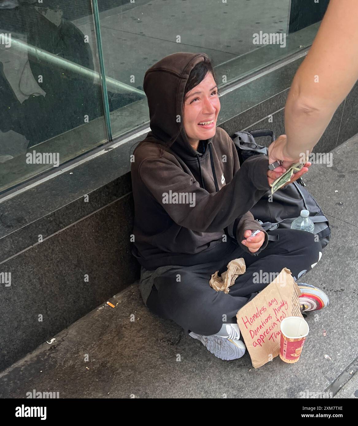 Obdachlose Frau zeigt sich emotional dank eines gbenerartigen Passanten auf der 5th Avenue in Midtown Manhattan, New York City. Stockfoto