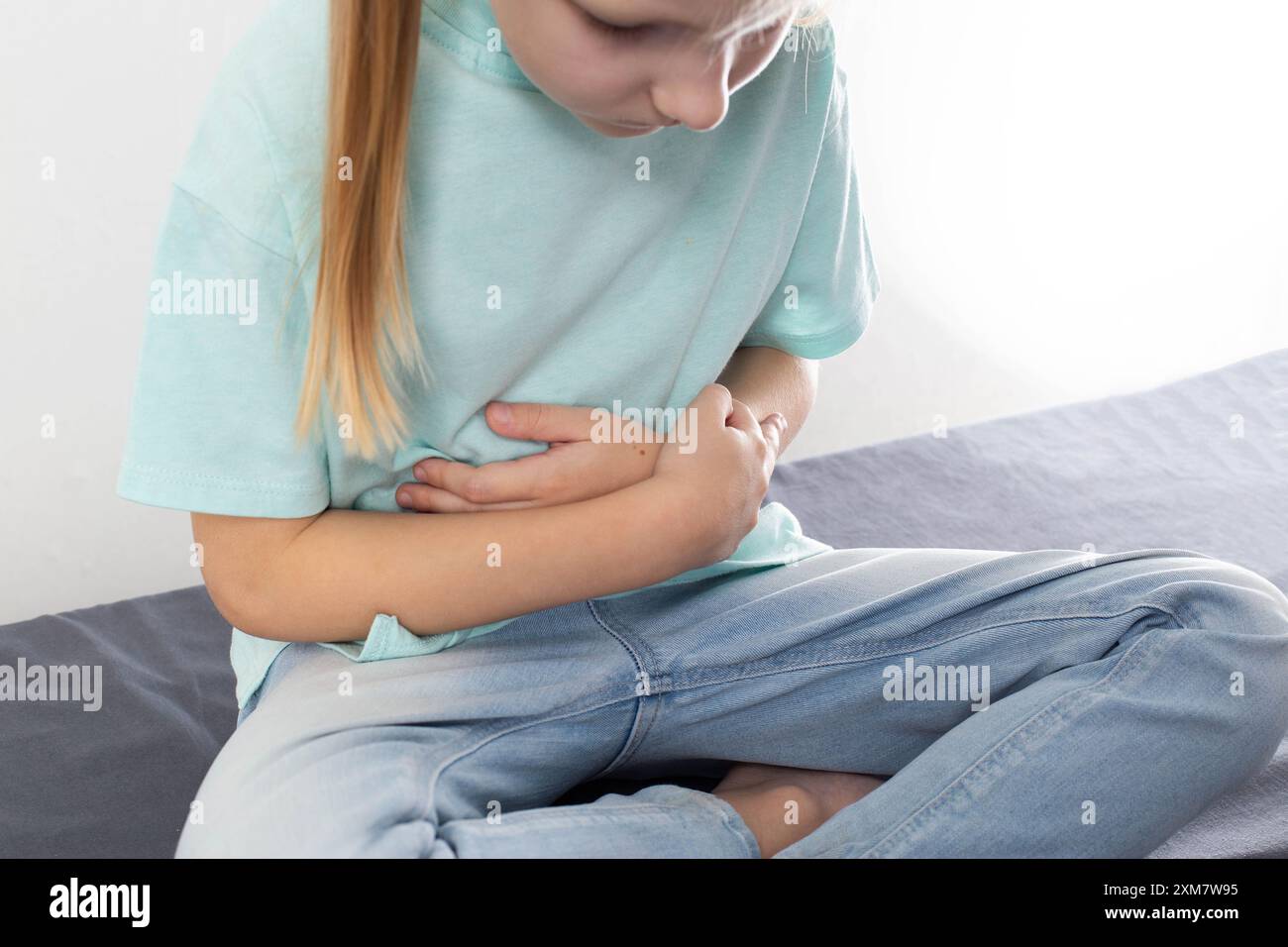 Ein siebenjähriges blondes Mädchen sitzt und hält ihren Bauch. Das Konzept der Bauchschmerzen bei Kindern aufgrund schlechter Ernährung. Verdauungsstörungen, Psychos Stockfoto