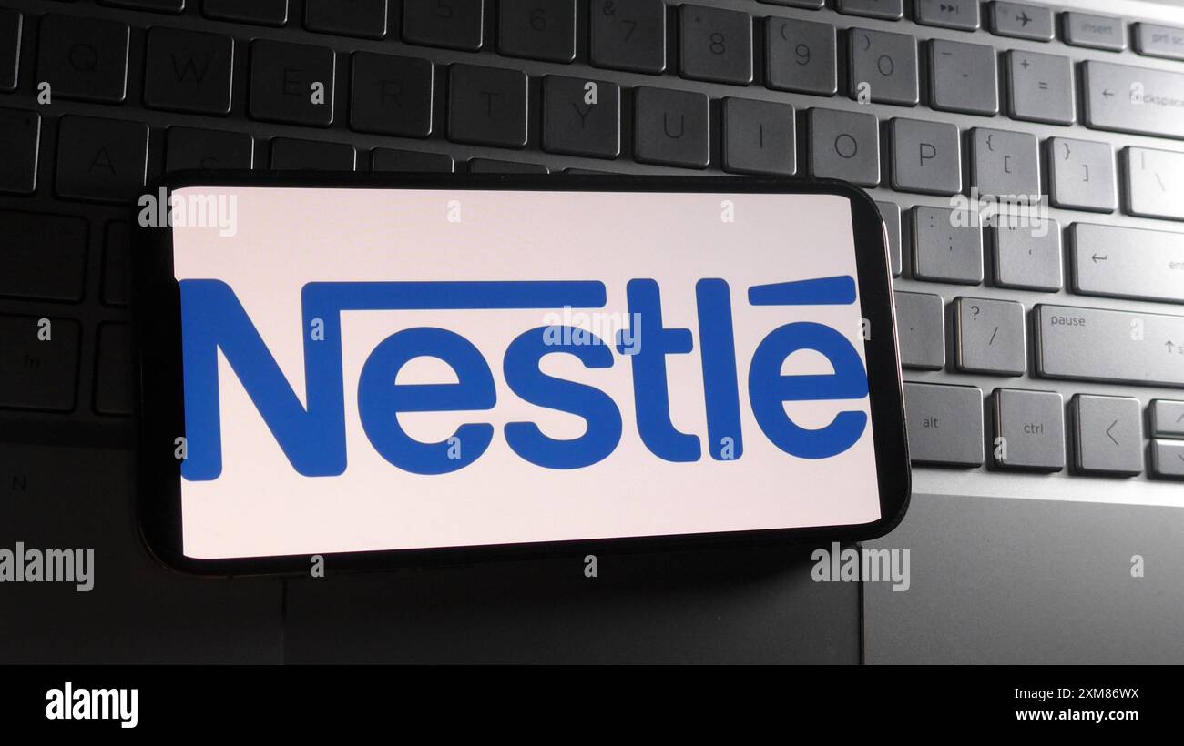 In dieser Fotoabbildung wird das Nestlé-Logo auf einem Smartphone mit Hintergrund einer Laptop-Tastatur angezeigt. Stockfoto