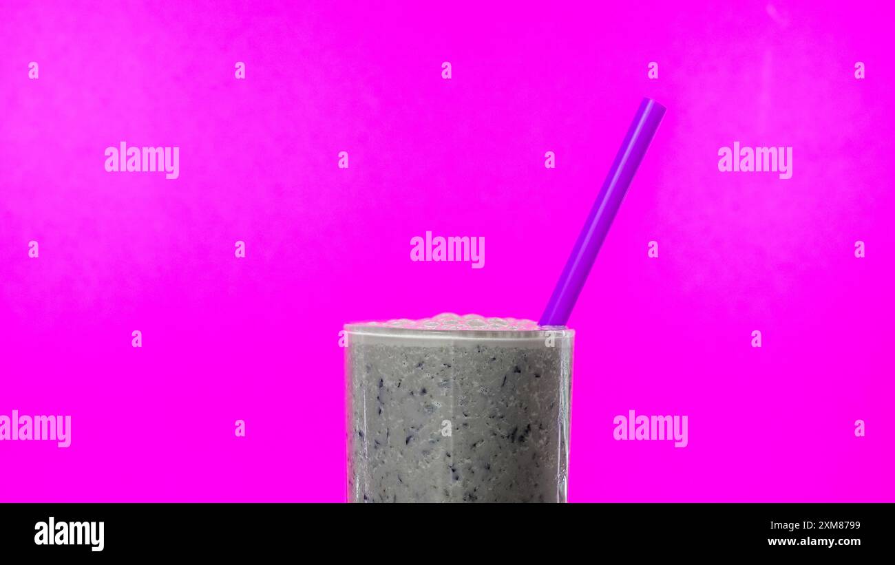 Neben frischen Blaubeeren wird ein Bananen- und Heidelbeeren-Smoothie mit violettem Strohhalm vor einem leuchtend rosa Hintergrund platziert Stockfoto