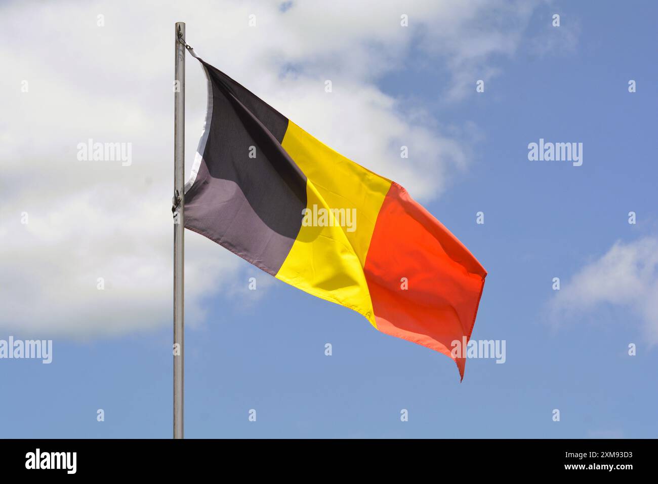 Die belgische Nationalflagge fliegt an einem schönen Sommertag mit blauem Himmel und weißen Wolken einen Fahnenmast hoch. Stockfoto