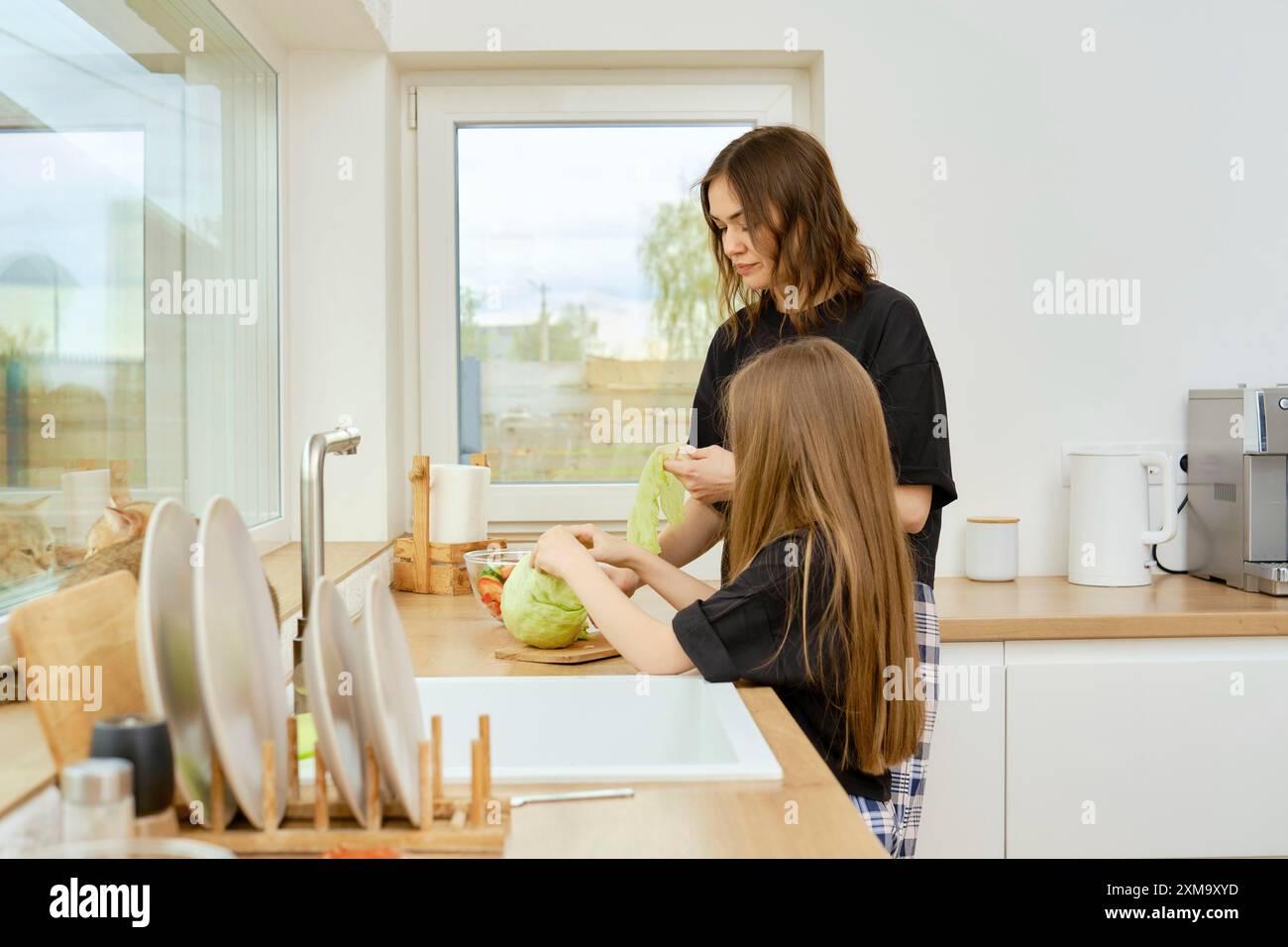 Mutter und Tochter reißen Eisbergsalatblätter vom Kopf, während sie in einer hell beleuchteten Küche stehen Stockfoto