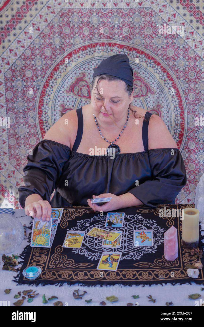 Eine Wahrsagerin in schwarz gekleidet liest die Tarotkarten, sagt die Zukunft, auf dem Tisch stehen Tarotkarten, Kerzen und Quarzsteine Stockfoto