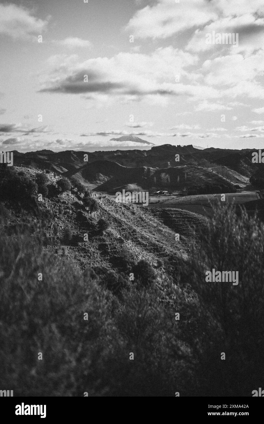 Schwarz-weiß-Foto von Hügeln und Bergen unter bewölktem Himmel, das eine ruhige und unasphaltierte Atmosphäre vermittelt, Mount Taranaki, Neuseeland Stockfoto