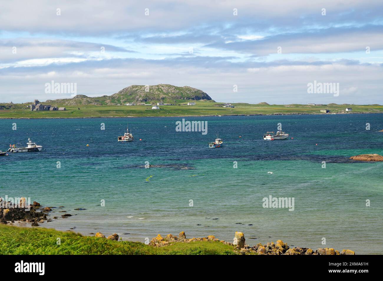 Mehrere Boote liegen im türkisblauen Wasser, mit grünen Hügeln und einer Insel im Hintergrund, Blick auf die heilige Insel Iona, Innere, Hebriden Stockfoto