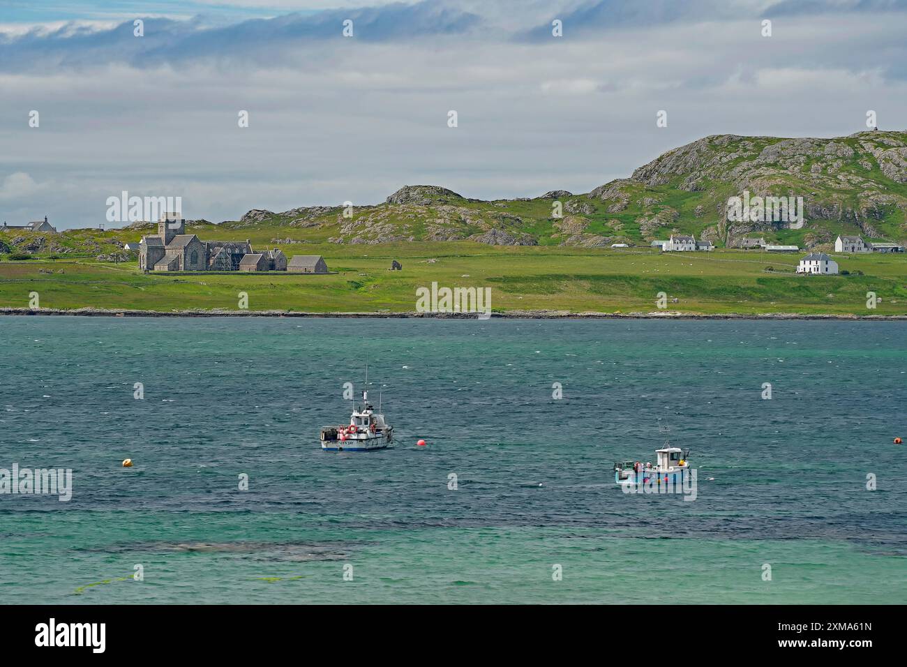 Mehrere Boote im Wasser vor einer grünen Insel mit einer Kirche und Hügeln im Hintergrund, Iona Abbey, heilige Insel, Iona, innen, Hebriden Stockfoto
