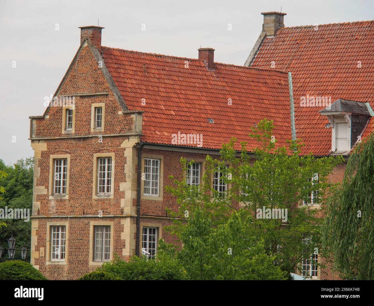 Altes historisches Backsteinhaus mit rotem Ziegeldach, umgeben von Bäumen, havixbeck, deutschland Stockfoto