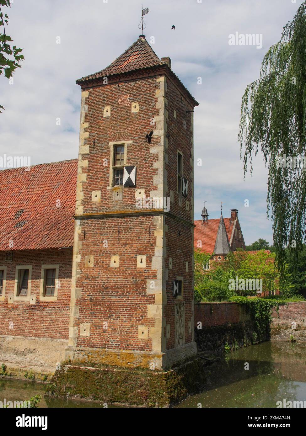 Backsteinturm mit rotem Dach und Wassergraben unter klarem Himmel, havixbeck, deutschland Stockfoto