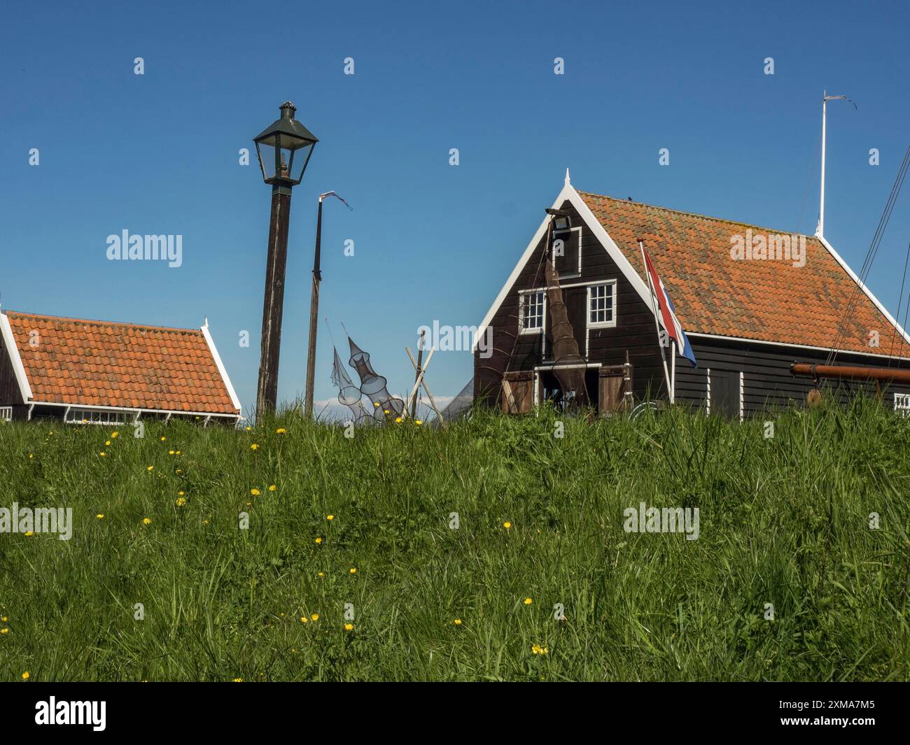 Schwarzes Gebäude mit Lampe und niederländischer Flagge umgeben von grüner Wiese, enkhuizen, niederlande Stockfoto