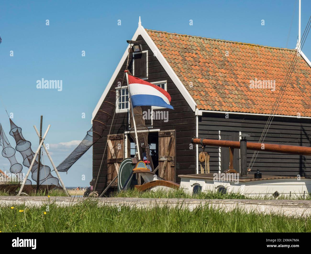 Schwarzes Gebäude mit niederländischer Flagge unter klarem blauem Himmel und grüner Wiese, enkhuizen, niederlande Stockfoto