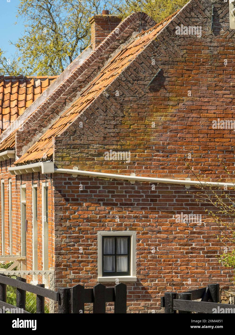 Ein historisches Backsteinhaus mit gekacheltem Dach und kleinem Fenster, umgeben von einem Holzzaun, enkhuizen, niederlande Stockfoto