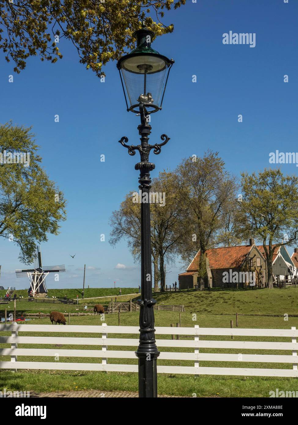 Eine alte Straßenlaterne, dahinter eine grüne Weide mit einer Windmühle und Häusern, enkhuizen, niederlande Stockfoto