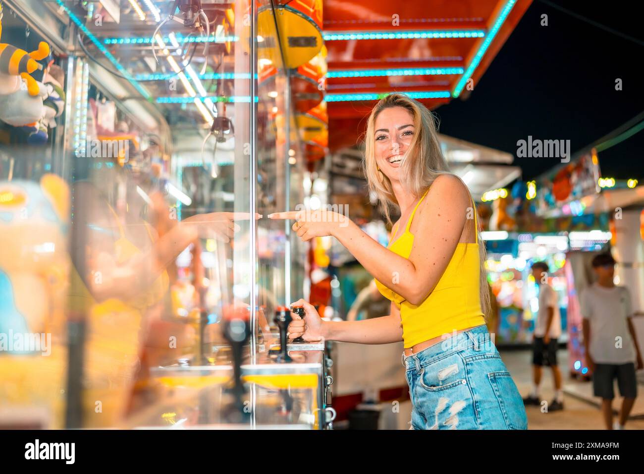 Glückliche blonde Frau, die nachts auf der Messe Arcade-Spiele spielt Stockfoto