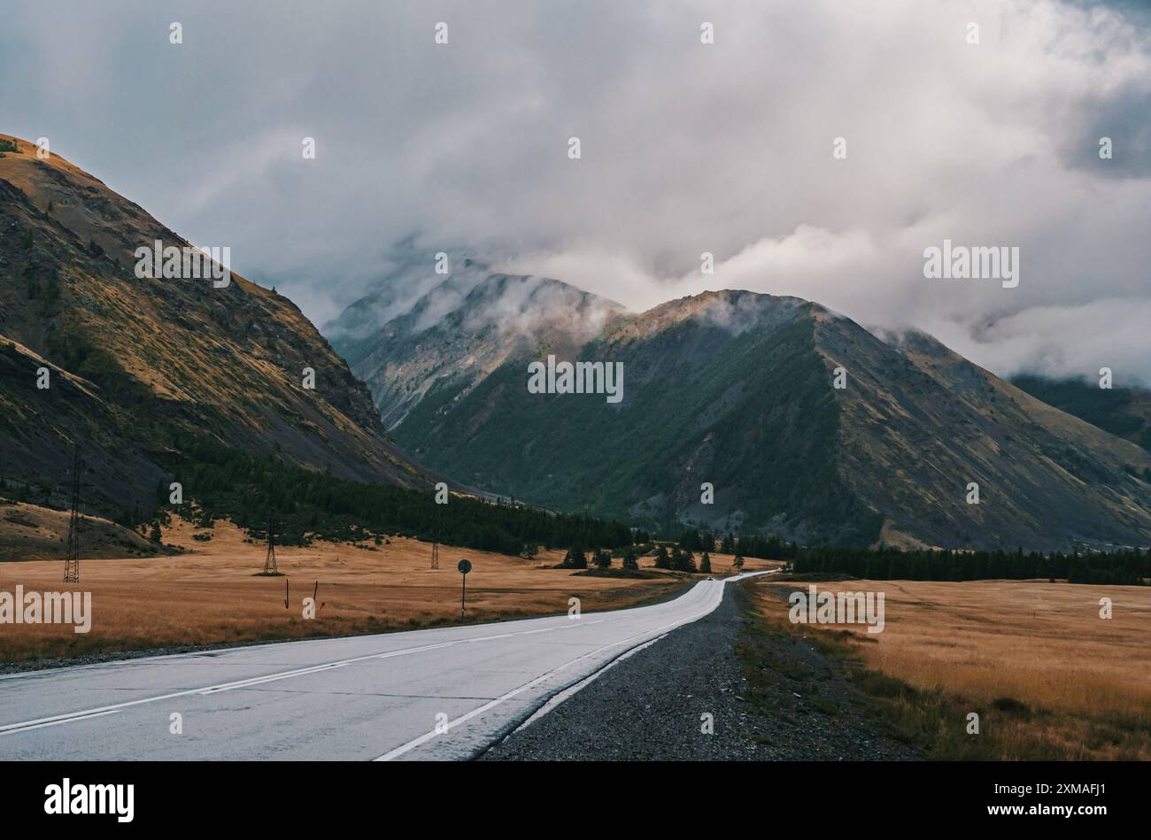 Majestätische Berge unter bewölktem Himmel entlang einer ruhigen Landstraße im Herbst Stockfoto