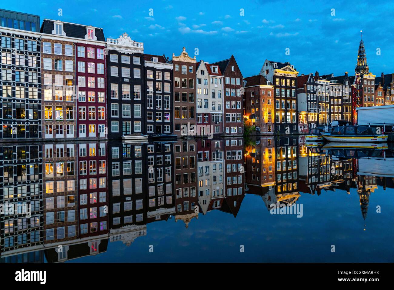 Kanalhäuser am Damrak, im Zentrum der Altstadt von Amsterdam, Hafen, Ausgangspunkt vieler Kanaltouren, abends Kirchturm von Stockfoto