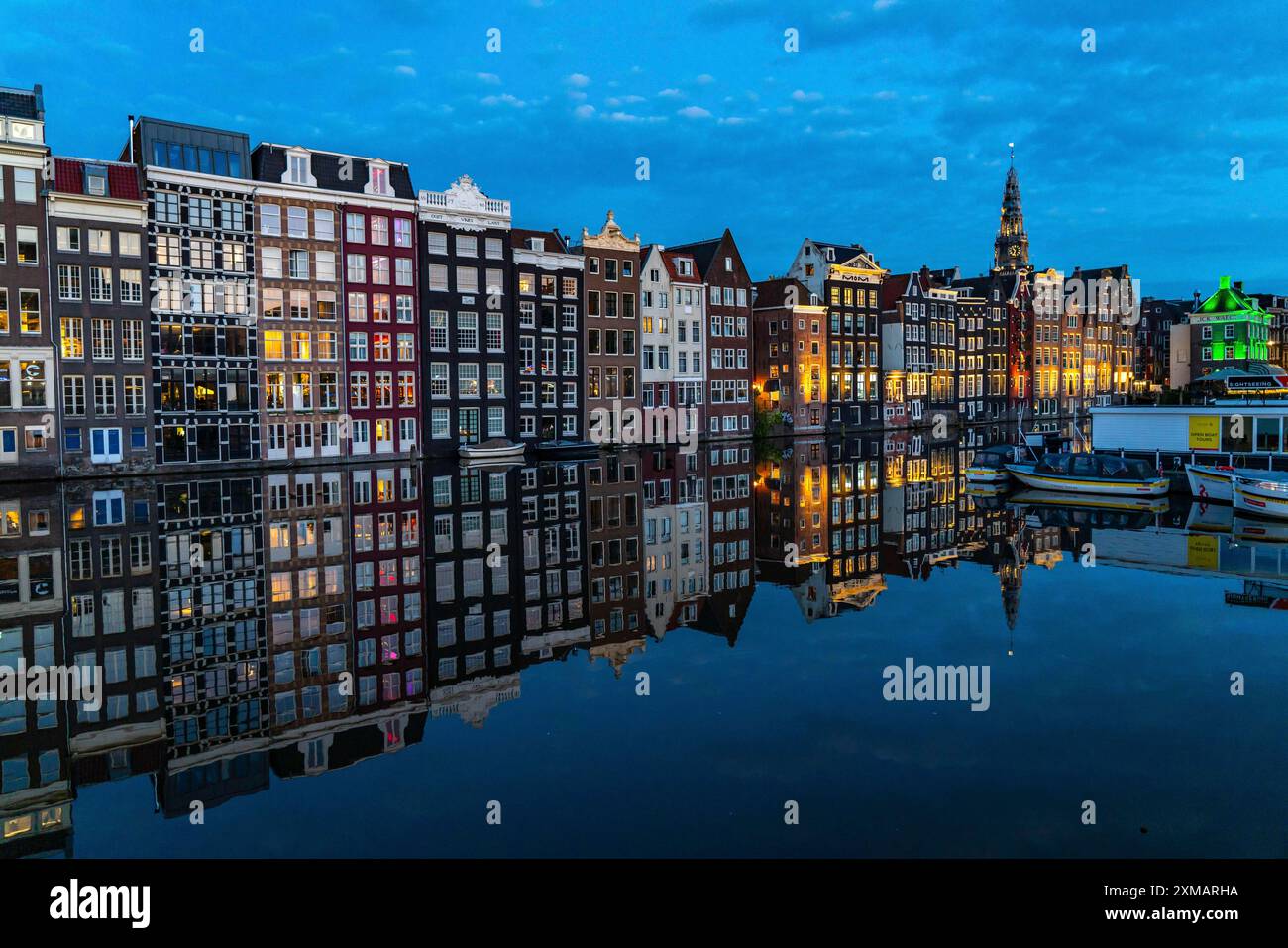 Kanalhäuser am Damrak, im Zentrum der Altstadt von Amsterdam, Hafen, Ausgangspunkt vieler Kanaltouren, abends Kirchturm von Stockfoto