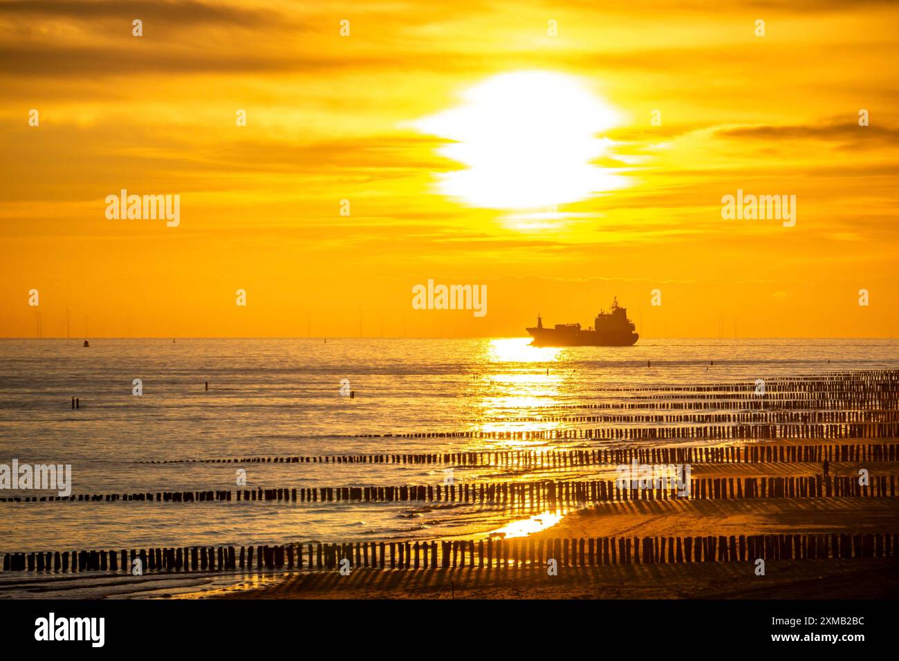 Sonnenuntergang am Strand von Zoutelande, Strand mit Holzpfahlbrüchen, Frachtschiff in Richtung Westerschelde, Zeeland, Niederlande Stockfoto