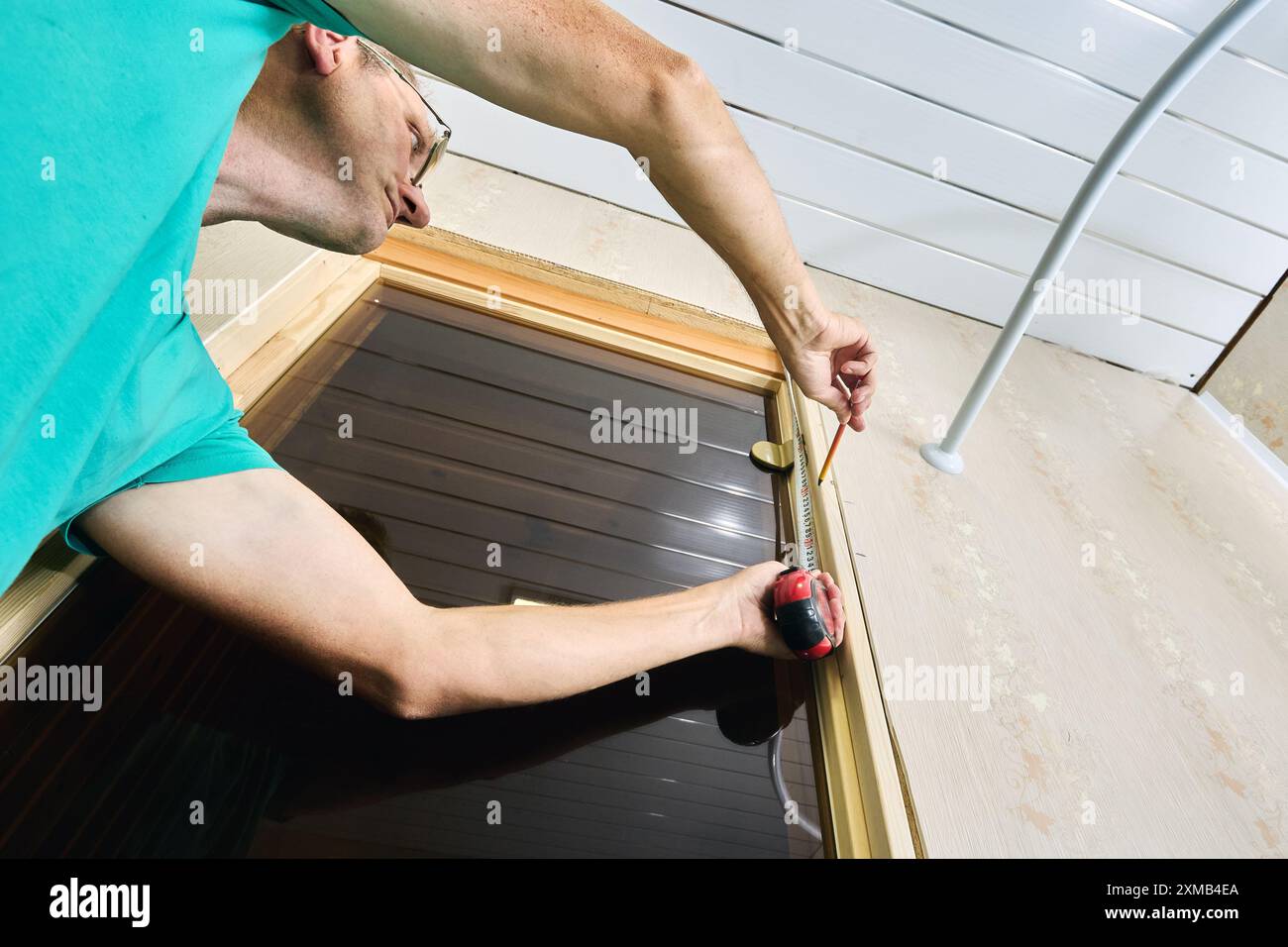 Der Zimmermann misst die Saunatüren vor dem Auskleiden des Strandes und verwendet zum Markieren ein Maßband und einen Bleistift. Stockfoto