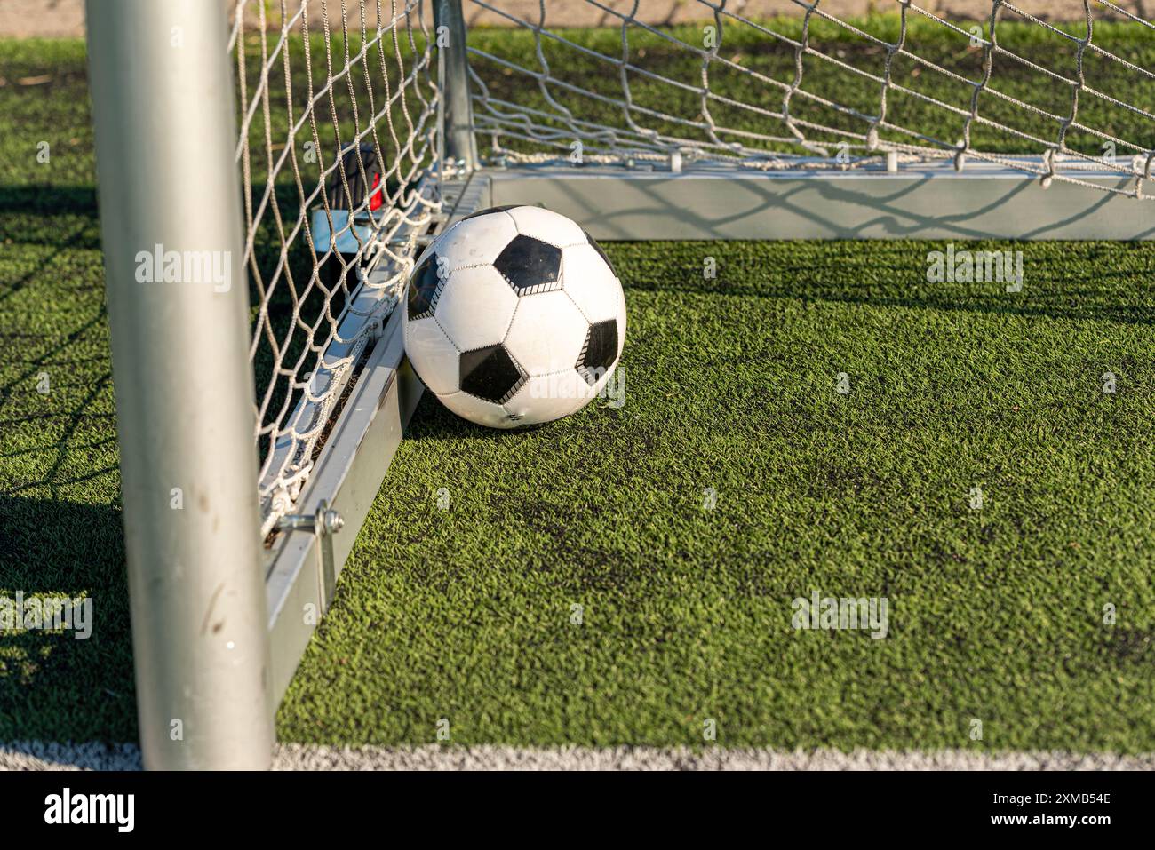 Ein schwarz-weißer Fußball, der durch einen kräftigen Schuss angetrieben wird und das Netz durchbricht, um ein perfektes Tor zu erzielen. Das wulstige Netz betont den Aufprall und die Qualität Stockfoto