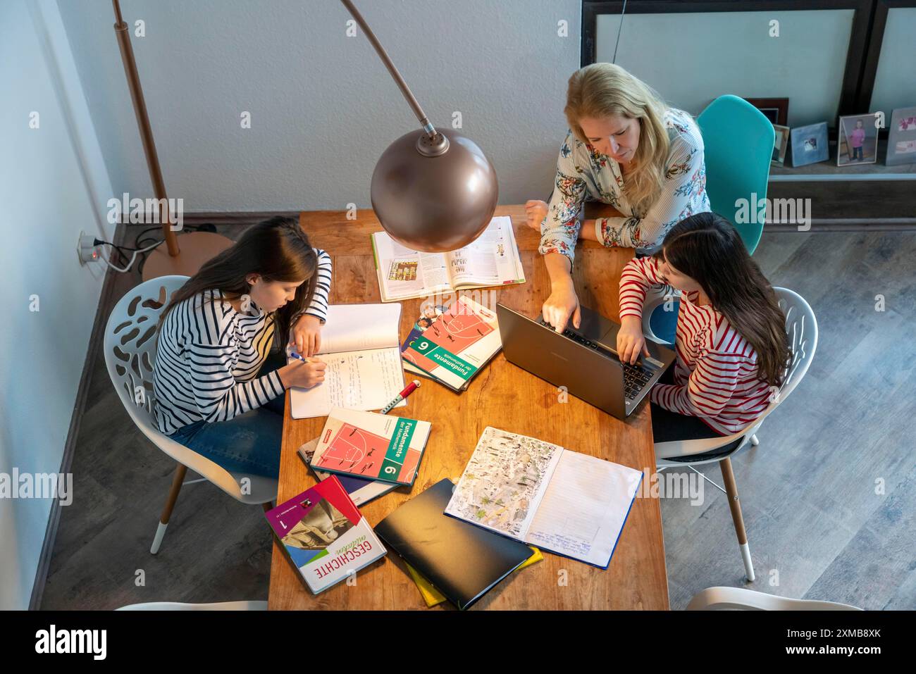 Während der Abriegelung im Januar 2021 hilft Mutter ihren beiden Töchtern zu Hause beim Lernen, mit Lehrbüchern und Computern, Schulschließungen Stockfoto