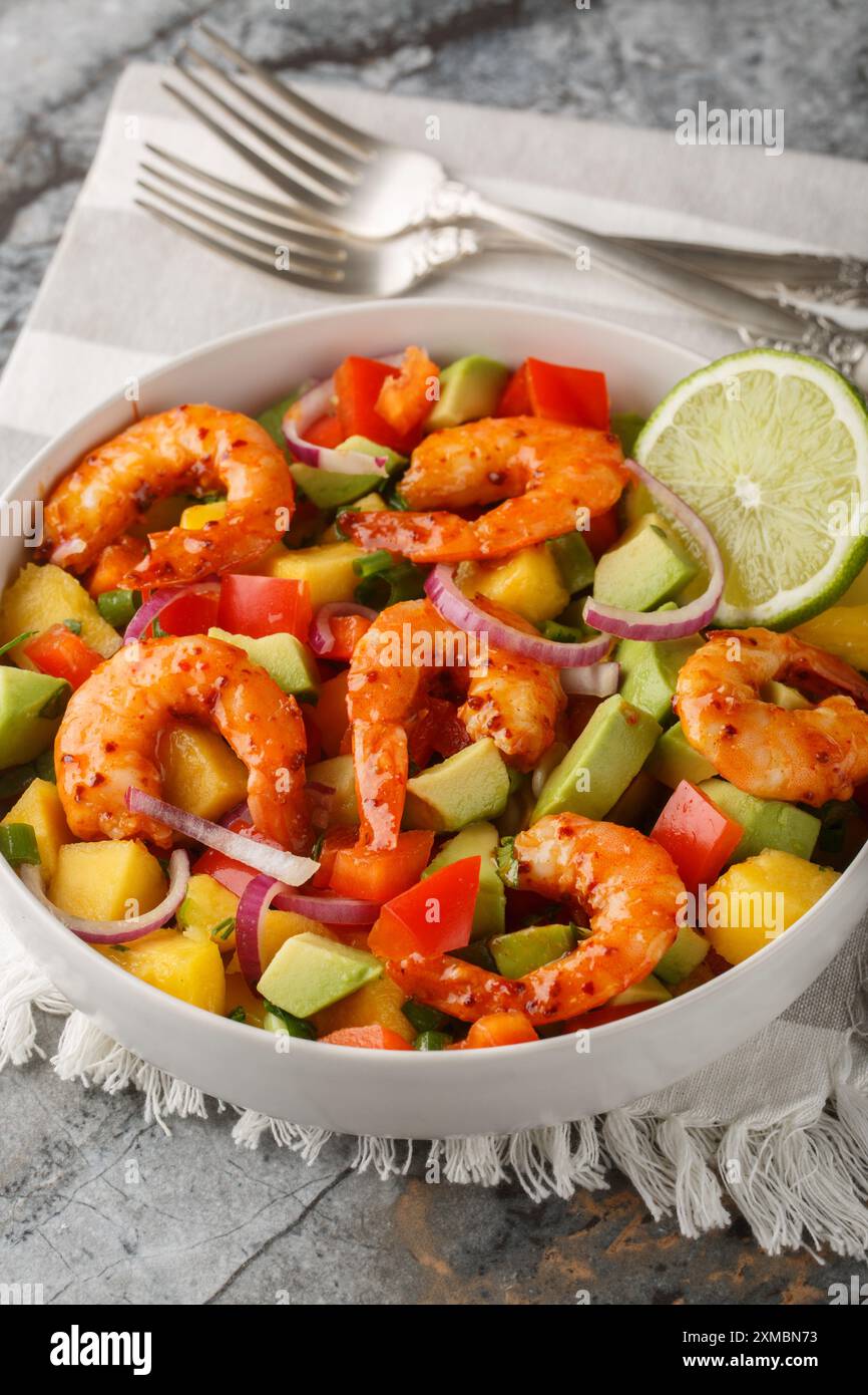 Erfrischender Mangogarnelen-Salat mit roten Zwiebeln, Paprika und Avocado in einer Schüssel auf dem Tisch. Vertikal Stockfoto