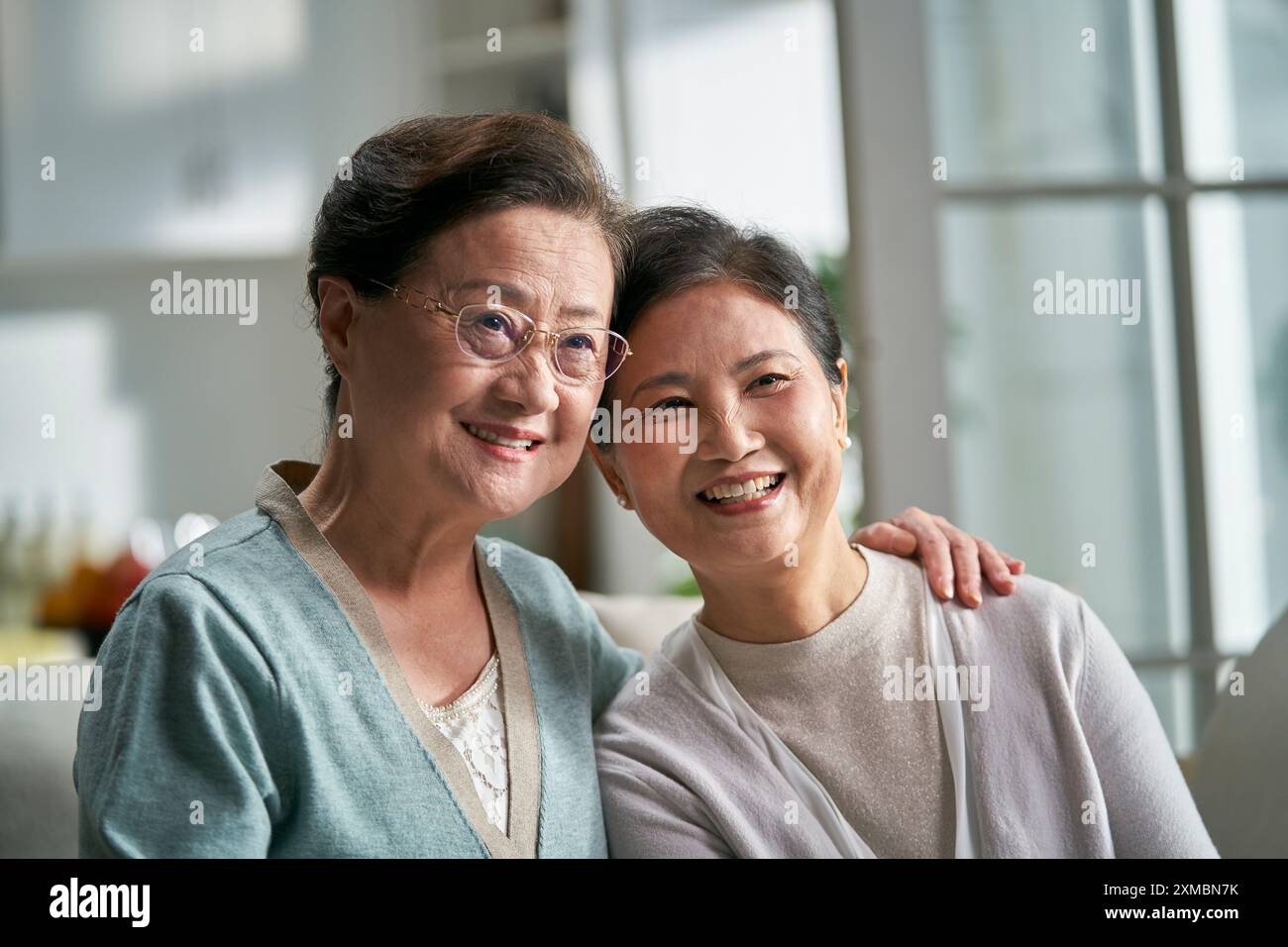 Porträt von zwei älteren asiatischen Frauen, die zu Hause glücklich und lächelnd auf der Couch sitzen Stockfoto