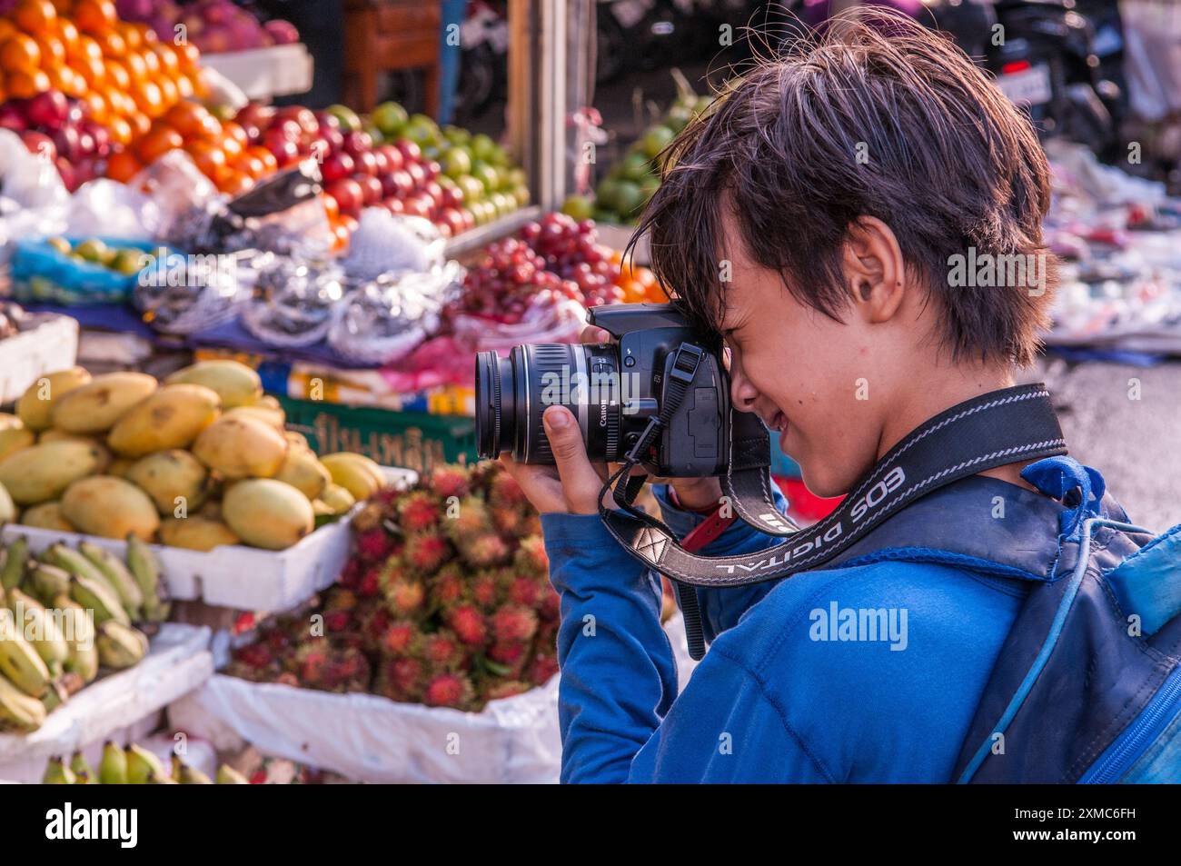 11 Jahre alter gemischter Rassenjunge (kambodschanisch-amerikanisch), der einen Obststand schießt. Der Russische Markt, Phnom Penh, Kambodscha. © Kraig Lieb Stockfoto