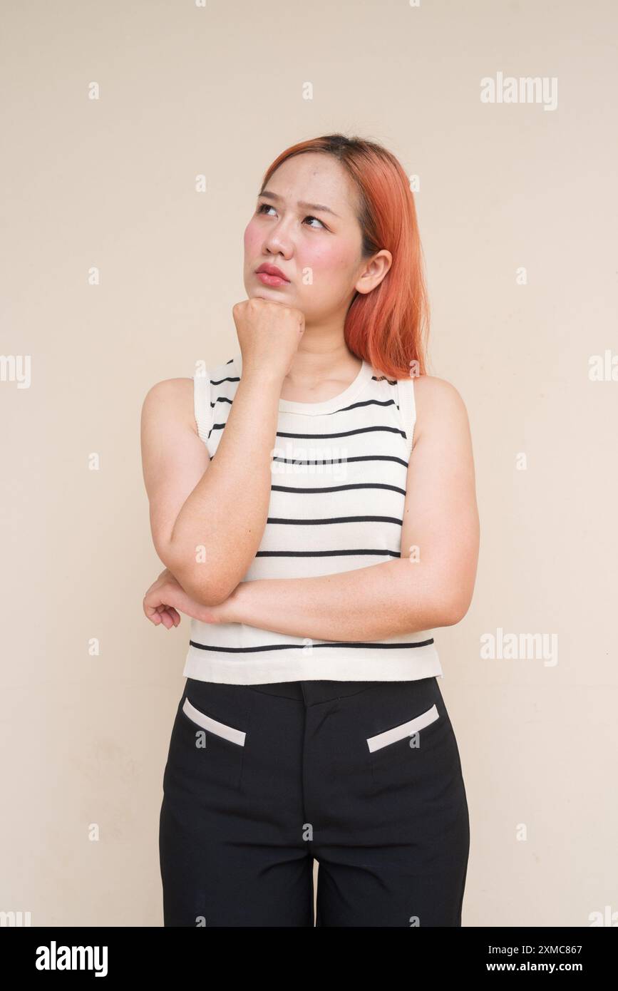 Porträt einer schönen asiatischen Frau, die vor dem Hintergrund des Plain Studio denkt Stockfoto