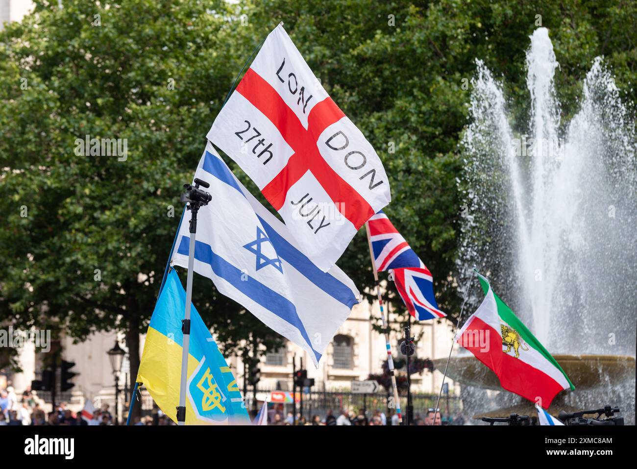 Trafalgar Square, Westminster, London, Großbritannien. Juli 2024. Anhänger von Tommy Robinson versammelten sich in The Strand vor den königlichen Justizgerichten zu einem protestmarsch zum Trafalgar Square. Themen des Protestes sind die Einwanderung, und ein von Stand Up to Rassiism organisierter gegensätzlicher Protest macht sich auf den Weg nach Whitehall, wo 1000 Polizisten zur Abschreckung von Zusammenstößen eingesetzt werden. Flaggen auf dem Trafalgar Square, mit englischer Flagge, israelischer Flagge, ukrainischer Flagge und iranischer Löwen- und Sonnenflagge, Datum vom 27. Juli Stockfoto