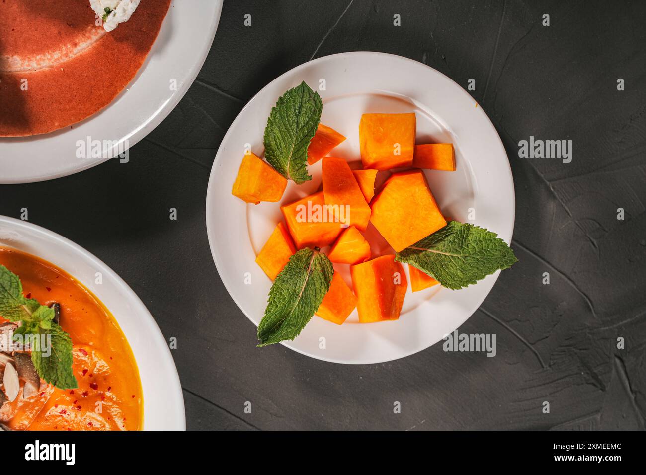 Kürbis mit Minze auf einem weißen Teller mit Gemüsesuppe, Kartoffelpüree und Pfannkuchen auf grauem, strukturiertem Hintergrund. Hochwertige Fotos Stockfoto