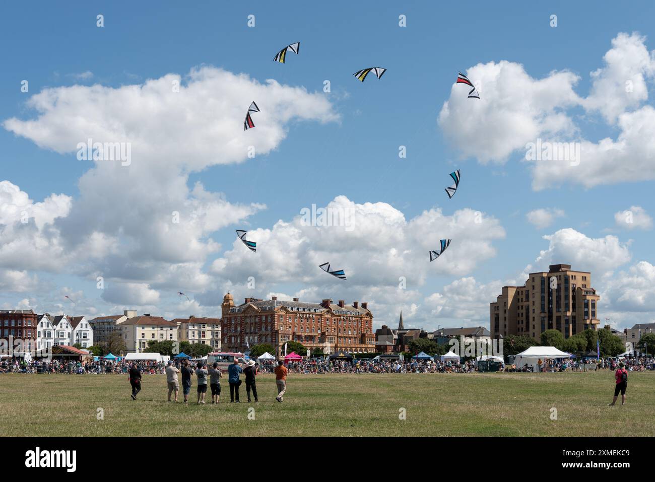 Drachenfest auf Southsea, das in Portsmouth verbreitet ist. Gruppe von Leuten, die Drachen in Formation vor dem Queens Hotel fliegen. Juli 2024. Stockfoto