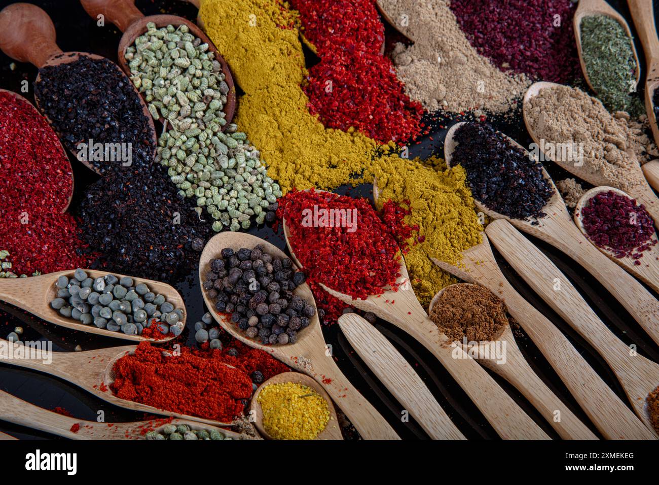 Große Sammlung von Gewürzen und Kräutern in Holzlöffeln. Gewürze für Lebensmittel auf schwarzem Hintergrund. Bunte Kräuter und Gewürze zum Kochen Stockfoto