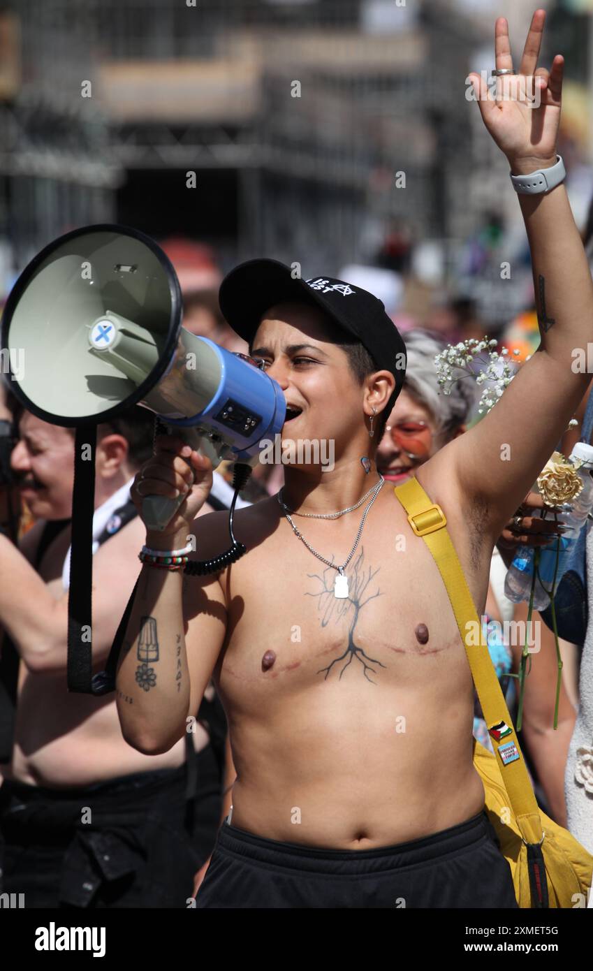 London, England, Großbritannien. Juli 2024. Eine Unterstützerin mit einer großen Narbe auf der Brust, die durch eine mögliche Mastektomie verursacht wurde, spricht die Parade während der Parade durch ein Megaphon an, während sie London durchquert. Das Thema der diesjährigen Parade ist "Gerechtigkeit und Befreiung", die für die Trans-Rechte und in Solidarität mit Palästina, Sudan, Haiti und Kongo steht. Quelle: ZUMA Press, Inc./Alamy Live News Stockfoto