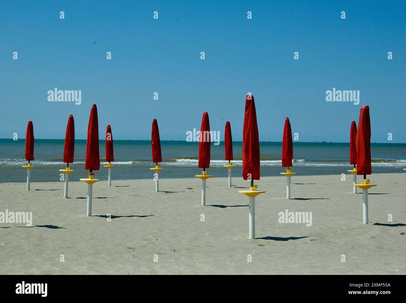 Leerer Strand mit feinem Sand und gefalteten roten Sonnenschirmen an der Adria in Italien im Sommer. Stockfoto