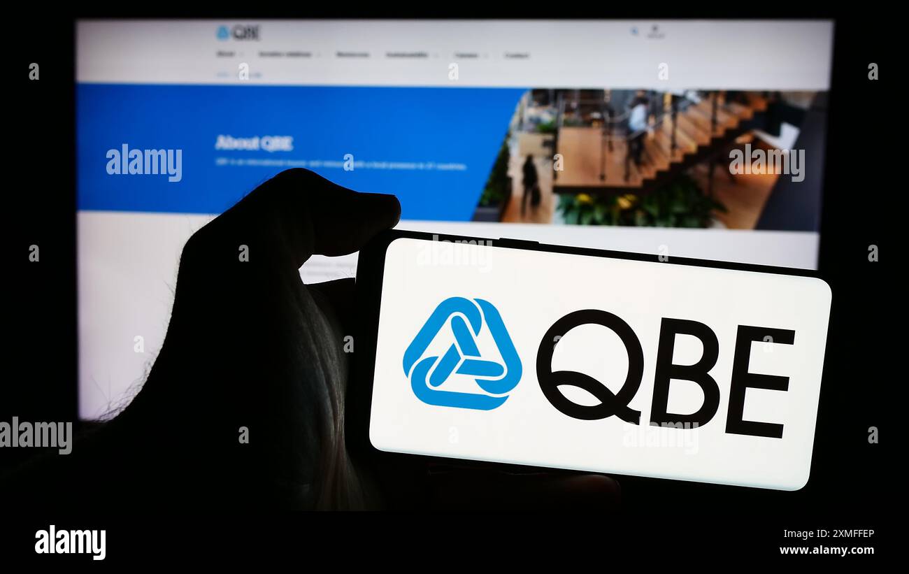 Person mit Smartphone und Logo des australischen Unternehmens QBE Insurance Group Limited vor der Website. Schwerpunkt auf dem Display des Telefons. Stockfoto