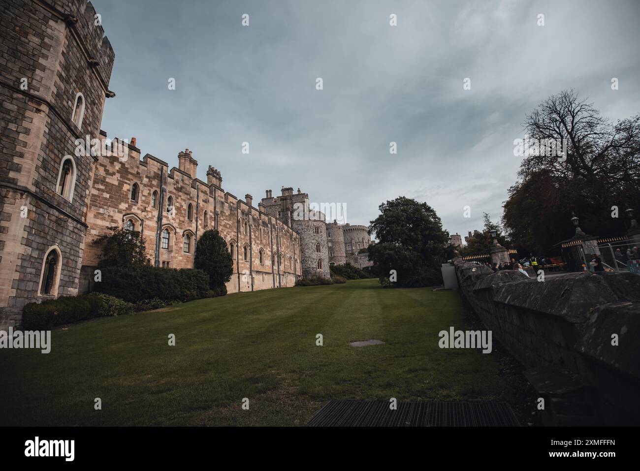 Windor Castle, Großbritannien - 16. Oktober 2023 : Eine Burgmauer aus Stein mit kleinen Fenstern überblickt ein grasbewachsenes Feld und ein Metallgitter. Stockfoto