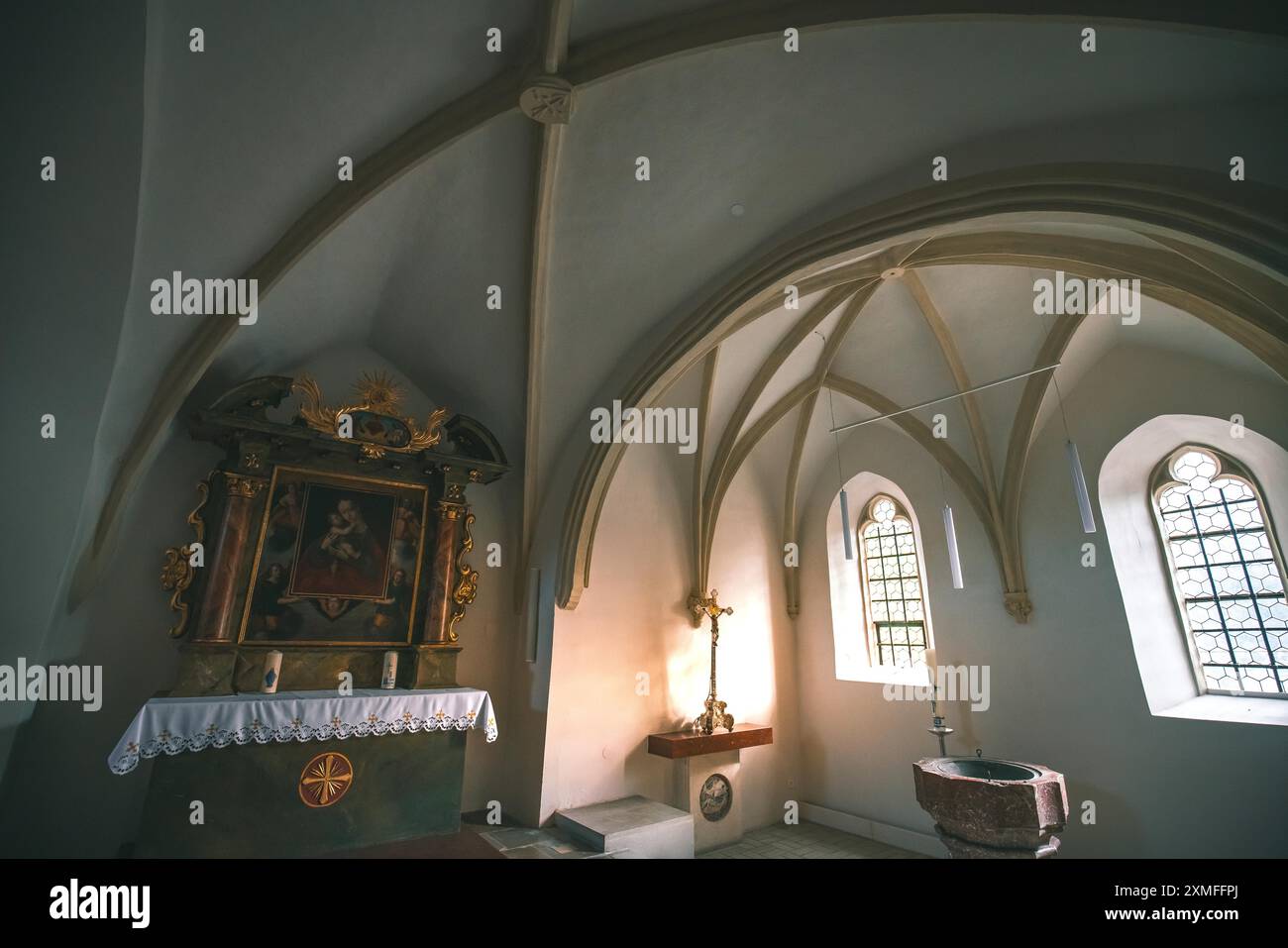 Österreich - 26. Oktober 2023 : Eine kleine, dunkle Kapelle mit gewölbter Decke, Buntglasfenster, einem kunstvollen Altar und einem Taufbecken. Stockfoto
